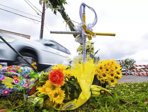 A collection of flowers and a cross with a halo are seen at the location where the body of Linda Frickey was recovered after she was carjacked and dragged to her death a day earlier on N. Pierce Street in New Orleans, Tuesday, March 22, 2022. Four teens accused in the dragging death of an elderly New Orleans woman whose arm was severed during a carjacking have pleaded not guilty. News outlets report the suspects — a 17-year-old boy, a 16-year-old girl and two 15-year-old girls — entered the 