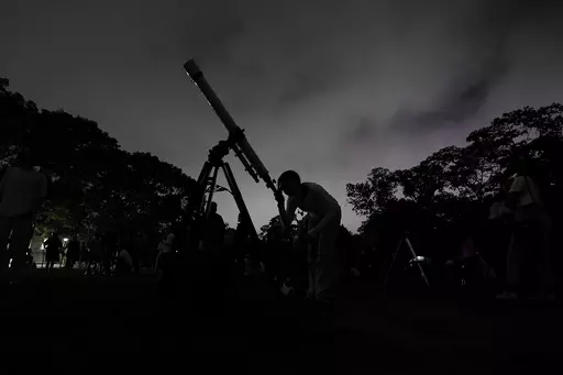 A girl looks at the moon through a telescope in Caracas, Venezuela, on Sunday, May 15, 2022. The best day to spot five planets, Mercury, Jupiter, Venus, Uranus and Mars, lined up in the night sky is Tuesday, March 28, 2023, right after sunset. The five-planet array will be visible from anywhere on Earth, as long as you have clear skies. (AP Photo/Matias Delacroix)