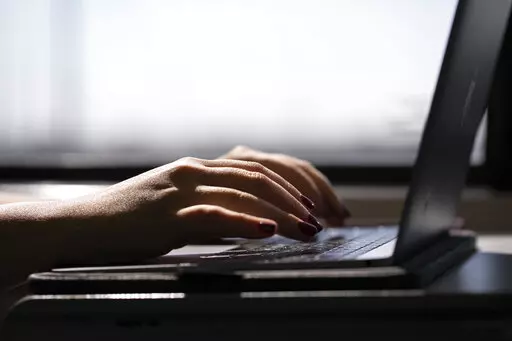 A woman types on a laptop while on a train in New Jersey, May 18, 2021. A trial of a four-day workweek in Britain, billed as the world's largest, has found that an overwhelming majority of the 61 companies that participated over six months last year will keep going with the shorter hours and that most employees were less stressed and burned out and had better work-life balance. (AP Photo/Jenny Kane, File)