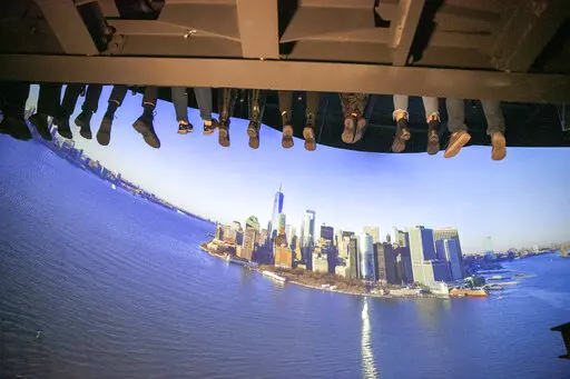 People ride a new indoor tourist attraction called RiseNY just off Times Square in Manhattan's Theater District in New York City on Tuesday, March 1, 2022. Visitors strap themselves into a row of seats and are lifted 30 feet off the ground inside a 180 degree, 40-foot projection dome to take a bird's eye virtual view of city landmarks and seasonal events. (AP Photo/Ted Shaffrey)