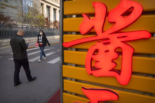 People wearing face masks walk in the Wangfujing shopping district in Beijing, Saturday, Nov. 19, 2022. Performances have been suspended at one of Beijing's oldest and most renowned theaters amid a new wave of shop and restaurant closures in response to a spike in COVID-19 cases in the Chinese capital. (AP Photo/Mark Schiefelbein)