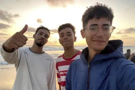In this undated photo provided by Helmi Hirez, Mohamed (Medo) Halimy, left, and twin brothers Mohammed Hirez, center, and Helmi Hirez, right, stand on a beach in Gaza. (Helmi Hirez via AP).