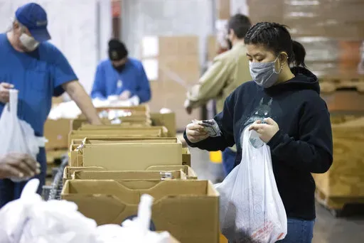 Volunteer Ana Willis fills a bag with food items for the backpack program at Feeding America food bank in Elizabethtown, Ky., Monday, Jan. 17, 2022. Food banks across the country are experiencing a critical shortage of volunteers as the omicron variant frightens people away from group activities. (AP Photo/Michael Clubb)