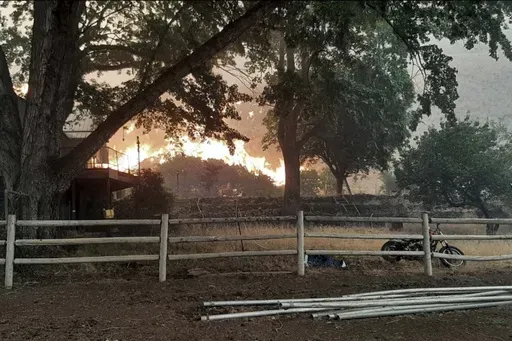 In this photo provided by Alison Oszman, a fast-moving wildfire near the Orego-Idaho border moves toward a home on Rye Valley Lane in Huntington, Ore., in the afternoon o fWednesday, July 24, 2024. (Alison Oszman via AP Photo)