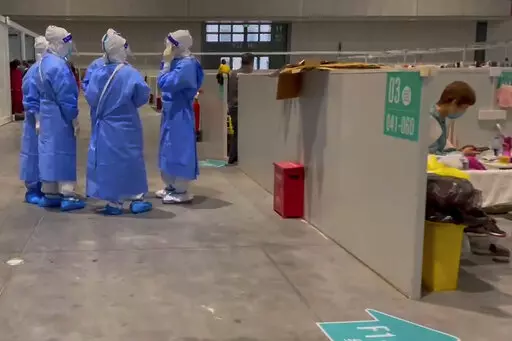 In this image taken from video provided by Beibei, who asked to be identified only by her given name, medical workers wearing protective suits chat as a resident takes a rest at the National Exhibition and Convention Center on April 15, 2022, in Shanghai.  The convention center converted to a quarantine facility set up for people who tested positive but have few or no symptoms. (Beibei via AP)