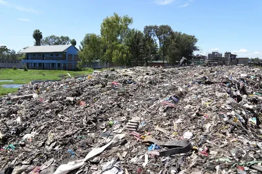 The Dandora Secondary school, separated with a mountain of garbage amidst smoke from burning trash at Dandora, the largest garbage dump in the capital Nairobi, Kenya Monday, April 22, 2024. Students at a school next to Kenya's largest dumpsite are on a mission to try to purify the air with bamboo. They have planted more than 100 seedlings along the wall that separates the school from the trash dump that was declared full 23 years ago. (AP Photo/Brian Inganga)