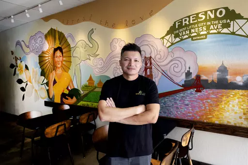 David Rasavong stands by a mural depicting his family's journey from Laos to San Francisco and then to Fresno, in his restaurant "Love & Thai" in Fresno, Calif. on Wednesday, Dec. 20, 2023. Rasavong's body still tenses up when recounting how a so-called animal welfare crusader in May implied on social media that his 7-month-old restaurant, Tasty Thai, owned a pitbull tied up at a home next door. What's more, the dog would eventually be meal fodder. By the next day, vitriolic comments, voicemails