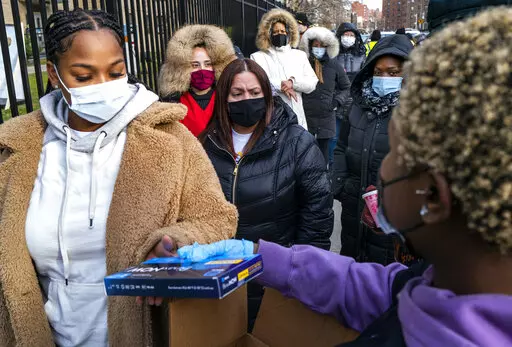 People line up and receive test kits to detect COVID-19 as they are distributed in New York on Dec. 23, 2021. The COVID-19 surge caused by the omicron variant means once-reliable indicators of the pandemic's progress are much less so, complicating how the media is able to tell the story. (AP Photo/Craig Ruttle, File)