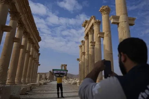 A member of the Syrian Civil Defense (White Helmets) takes a photo of his colleague holding the new Syrian flag at the ancient city of Palmyra, Syria, Saturday, Jan. 25, 2025. (AP Photo/Khalil Hamra)