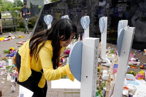 Yesenia Hernandez, granddaughter to Nicolas Toledo, who was killed during Monday's Highland Park., Ill., Fourth of July parade, writes on a memorial for Toledo along with the six others who lost their lives in the mass shooting, Wednesday, July 6, 2022, in Highland Park. (AP Photo/Charles Rex Arbogast)