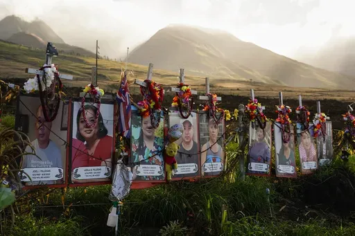 Photos of victims are displayed under white crosses at a memorial for victims of the August 2023 wildfire, above the Lahaina Bypass highway, Dec. 6, 2023, in Lahaina, Hawaii. (AP Photo/Lindsey Wasson, File)