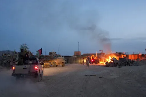 An Afghan National Army pickup truck passes parked U.S. armored military vehicles, as smoke rises from a fire in a trash burn pit at Forward Operating Base Caferetta Nawzad, Helmand province south of Kabul, Afghanistan, April 28, 2011. The Senate is expected to approve on Thursday a large expansion of health care and disability benefits for veterans of Iraq and Afghanistan in response to concerns about their exposure to toxic burn pits.  (AP Photo/Simon Klingert, File)