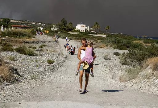 A man carries a child as they leave an area where a forest fire burns, on the island of Rhodes, Greece, Saturday, July 22, 2023. A large wildfire burning on the Greek island of Rhodes for a fifth day has forced authorities to order an evacuation of four locations, including two seaside resorts. (Lefteris Diamanidis/InTime News via AP)