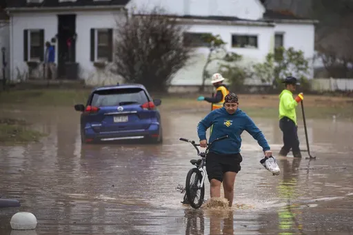 Siquoia Jackson, of Huntington, pulls a bike through the floodwater while trying to travel through the Enslow Park neighborhood on Thursday, Feb. 6, 2025, in Huntington, W.Va. (Ryan Fischer/The Herald-Dispatch via AP)