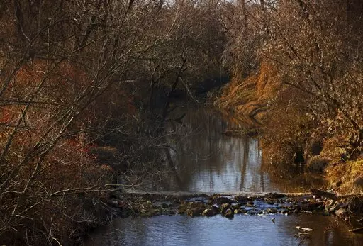 Water flows in Coldwater Creek on Thursday, Dec. 9, 2021, behind a row of homes at Belcroft Drive and Old Halls Ferry Road in Missouri's St. Louis County. Environmental investigation consultants have found significant radioactive contamination at an elementary school, which sits in the flood plain of Coldwater Creek which was contaminated by nuclear waste from weapons production during World War II. (Christian Gooden/St. Louis Post-Dispatch via AP)