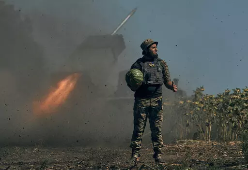A Ukrainian soldier holds a watermelon and thumbs up as a rocket launch system fires in the font line in Donetsk region, eastern Ukraine, Saturday, Aug. 3, 2022. (AP Photo/Kostiantyn Liberov)