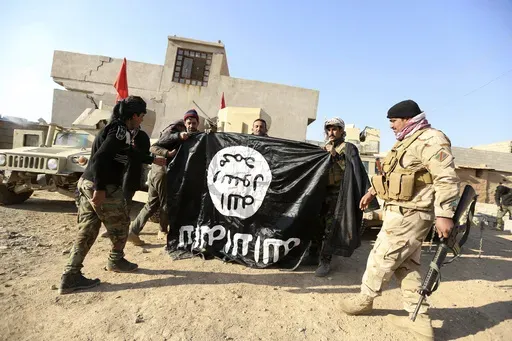 Iraqi Army soldiers celebrate as they hold a flag of the Islamic State group they captured during a military operation to regain control of a village outside Mosul, Iraq, Nov. 29, 2016. Ten years after the Islamic State group declared its caliphate in large parts of Iraq and Syria, the extremists now control no land, have lost many prominent founding leaders and are mostly away from the world news headlines. (AP Photo/Hadi Mizban, File)
