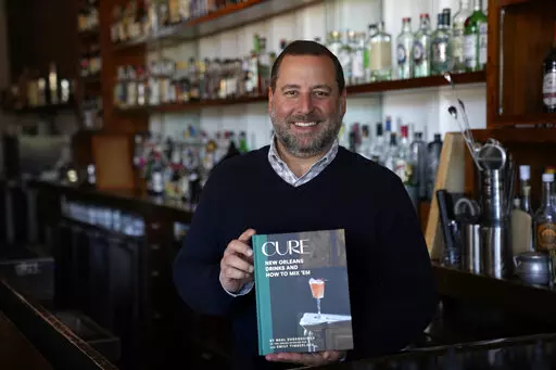 Neal Bodenheimer, owner and founder of Cure, poses in his craft cocktail bar with a copy of his new book "Cure: New Orleans Drinks and How to Mix 'Em" in New Orleans, Friday, Nov. 18, 2022. (AP Photo/Gerald Herbert)