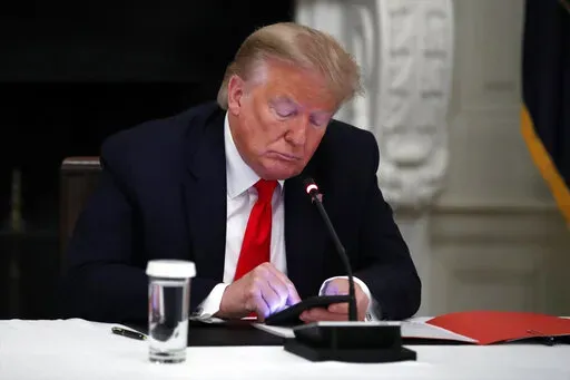 In this Thursday, June 18, 2020 file photo, President Donald Trump looks at his phone during a roundtable with governors on the reopening of America's small businesses, in the State Dining Room of the White House in Washington. On Wednesday, Jan. 25, 2023, Facebook parent Meta said in a blog post it is reinstating former President Trump’s personal account after two-year suspension following the Jan. 6 insurrection. (AP Photo/Alex Brandon, File)