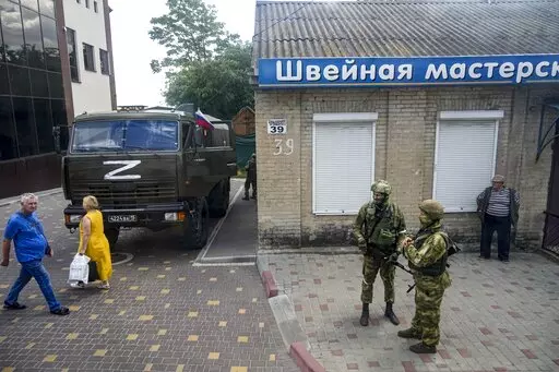 Russian soldiers guard an office for Russian citizenship applications as their military truck is parked nearby, in Melitopol, south Ukraine, on July 14, 2022. As Russians seized parts of eastern and southern Ukraine in the 8-month-old war, mayors, civilian administrators and others, including nuclear power plant workers, say they have been abducted, threatened or beaten to force their cooperation. In some instances, they have been killed. Human rights activists say these actions could constitute