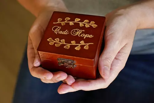 Abi Frazier holds a box containing an urn with the ashes of her daughter Cadi Hope, Thursday, Aug. 18, 2022, in Mustang, Okla. Frazier discovered at her 20-week anatomy scan that the baby she was carrying had a neural tube defect and other problems her doctors said were "incompatible with life." So she made the most difficult decision of her life last year: to terminate a much-wanted pregnancy. (AP Photo/Sue Ogrocki)