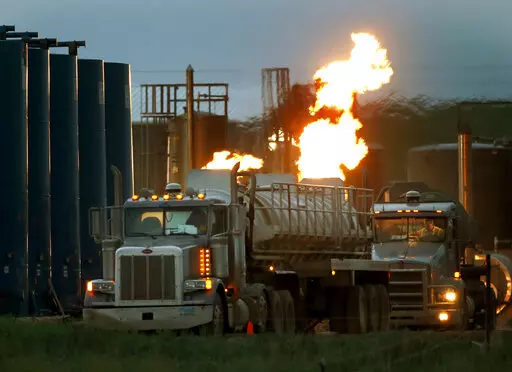 Drivers and their tanker trucks capable of hauling water and hydraulic fracturing liquid line up near a natural gas burn off flame and storage tanks in Williston, N.D., on June 9, 2014. Under new rules proposed by the Securities and Exchange Commission on Monday, March 21, 2022, companies would be required to disclose the greenhouse gas emissions they produce and how climate risk affects their business, as part of a drive across the government to address climate change. (AP Photo/Charles Rex Arb
