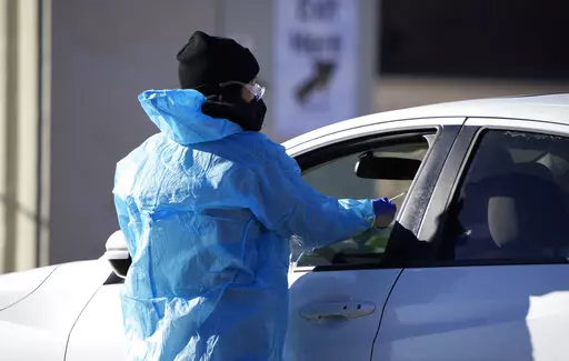 A medical technician performs a nasal swab test on a motorist queued up in a line at a COVID-19 testing site near All City Stadium Dec. 30, 2021, in southeast Denver. Millions of workers whose jobs don’t provide paid sick days are having to choose between their health and their paycheck as the omicron variant of COVID-19 rages across the nation. While many companies instituted more robust sick leave policies at the beginning of the pandemic, those have since been scaled back with the rollout o