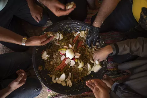 Palestinians eat "Lasima," a dish that is popular in the southern Gaza Strip but shunned in its north, at a garden in Khuzaa, Gaza Strip, Saturday, May 20, 2023. Locals call it "watermelon salad." But this seasonal delicacy is far from the sweet, refreshing taste the name evokes. (AP Photo/Fatima Shbair)