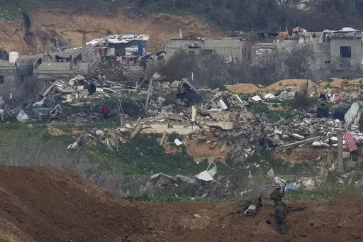 A Palestinian man wearing a red shirt, left, stands amidst the rubble of destroyed buildings, watching Israeli soldiers, bottom right, take position in the northern Gaza Strip, as seen from southern Israel, Sunday, Feb. 9, 2025. (AP Photo/Ohad Zwigenberg)