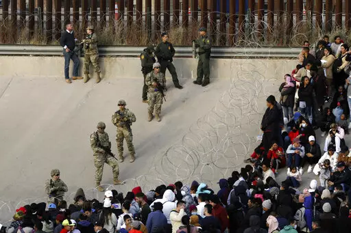 Migrants congregate on the banks of the Rio Grande at the U.S. border with Mexico on Tuesday, Dec. 20, 2022, where members of the Texas National Guard cordoned off a gap in the U.S. border wall. Restrictions that prevented many from seeking asylum in the U.S. remained in place beyond their anticipated end. (AP Photo/Morgan Lee)