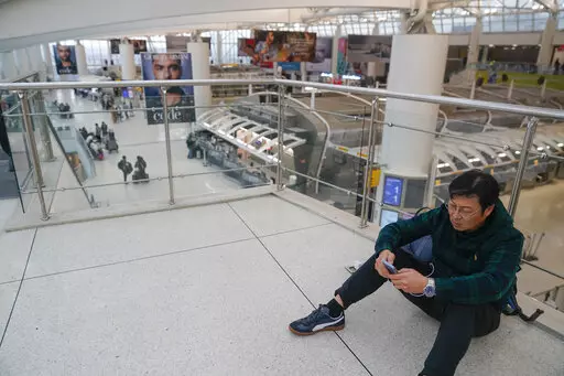 A man checks his phone in a mostly empty Terminal 1 at John F. Kennedy International Airport in New York, Friday, Feb. 17, 2023. A power outage in the terminal has stretched into a second day. The outage has stranded passengers and forced flights to be canceled or diverted to other airports. (AP Photo/Seth Wenig)
