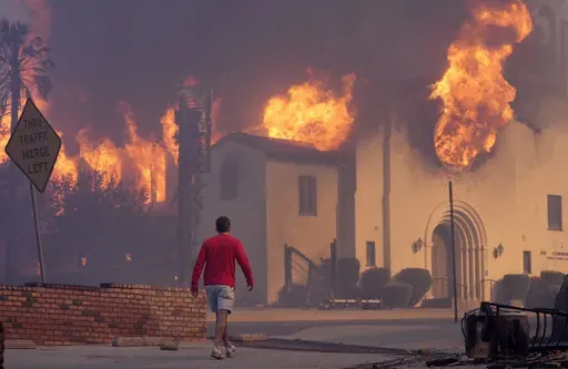 A man walks in front of the burning Altadena Community Church, Wednesday, Jan. 8, 2025, in the downtown Altadena section of Pasadena, Calif. (AP Photo/Chris Pizzello)