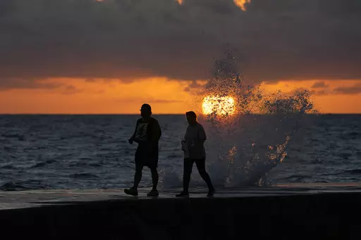 The sun rises above the Atlantic Ocean as waves crash near beach goers walking along a jetty, Dec. 7, 2022, in Bal Harbour, Fla. The world's oceans have suddenly spiked much hotter and well above record levels, with scientists trying to figure out what it means and whether it forecasts a surge in atmospheric warming. (AP Photo/Wilfredo Lee, File)
