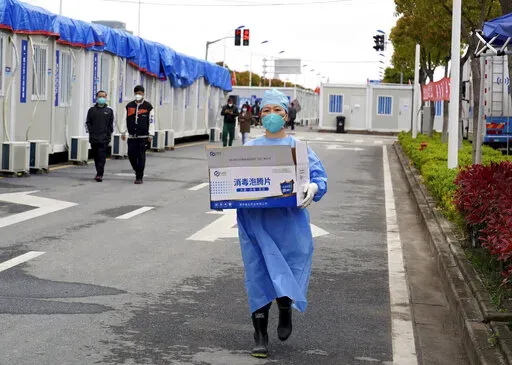 In this photo released by China's Xinhua News Agency, a worker carries a box of supplies at a makeshift hospital in Shanghai, China, Friday, April 15, 2022. Anti-virus controls that have shut down some of China's biggest cities and fueled public irritation are spreading as infections rise, hurting a weak economy and prompting warnings of possible global shockwaves. (Yang Youzong/Xinhua via AP)