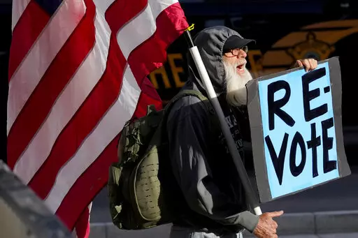 A man protests outside the Maricopa County Board of Supervisors auditorium prior to the board's general election canvass meeting, Nov. 28, 2022, in Phoenix. Worries that rogue county officials could undermine election results by refusing to certify them have lessened significantly in the wake of the midterms, with a lone Arizona county as the exception. Still, baseless attacks on the accuracy of the election by Republican county officials and angry members of the public already are raising conce