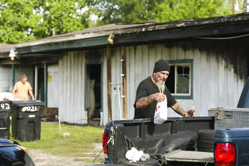 Robin Ahrens, a resident of a multi-room renting facility, walks past the burned out building in the aftermath of a fatal shooting in Houston on Sunday, Aug. 28, 2022. A longtime tenant started several fires at the site early Sunday and then shot at residents as they fled the blaze, before authorities fatally shot him, police said. (Brett Coomer/Houston Chronicle via AP)