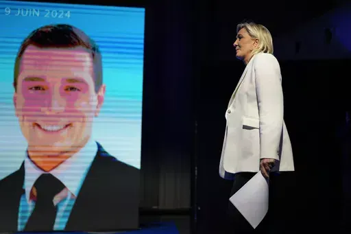 French far-right leader Marine Le Pen walks past a screen showing the president of the French far-right National Rally Jordan Bardella at the party election night headquarters after French President Emanuel Macron announced he dissolves National Assembly and calls new legislative election after defeat in EU vote, Sunday, June 9, 2024 in Paris. First projected results from France put far-right National Rally party well ahead in EU elections, according to French opinion poll institutes. (AP Photo/