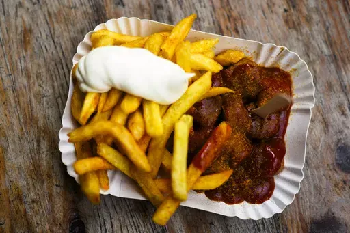 Currywurst, Germany's sausage with curry sauce, served on a cardboard platter with French fries and mayonnaise at Konnopke's Imbiß, a fast-food joint under the tracks at the Eberswalder Straße U-Bahn station, in Berlin, Germany, Friday, May 24, 2024. The currywurst promises to be among the most tantalizing gourmet treats on offer at the European Championship this summer. The currywurst is considered a fast-food delicacy in a country where the humble sausage enjoys great importance. (AP Photo/M