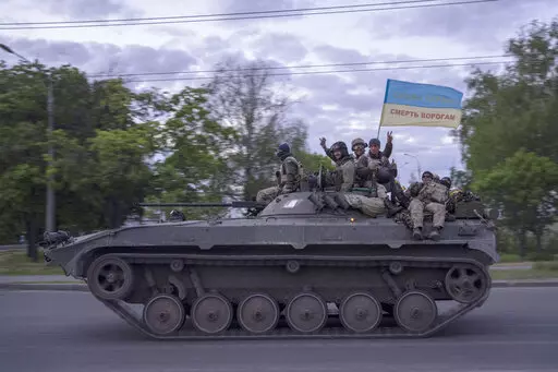 Ukrainian serviceman wave a flag with writing reading in Ukrainian "Glory to Ukraine", top, and "Death to the enemies"        as they ride atop of a tank in the Kharkiv region, eastern Ukraine, Monday, May 16, 2022. (AP Photo/Bernat Armangue)
