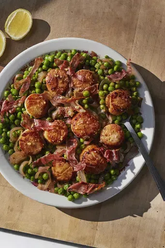 This image released by Weldon Owen shows a recipe for scallops with peas and prosciutto from the cookbook "Out There: A Camper Cookbook: Recipes from the Wild" by Lee Kalpakis. (Brittany Barb/Weldon Owen via AP)
