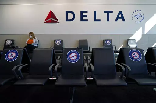 A passenger wears a face mask as she waits in a socially-distance area for a Delta Airlines flight, Wednesday, Feb. 3, 2021, at Hartsfield-Jackson International Airport in Atlanta.  Delta Air Lines will start paying flight attendants during the time that passengers are boarding. That's a first for a major U.S. airline. Flight attendants in the U.S. generally don't begin getting paid until the doors close after boarding. Delta said Tuesday, April 26, 2022, that the change will take effect in June