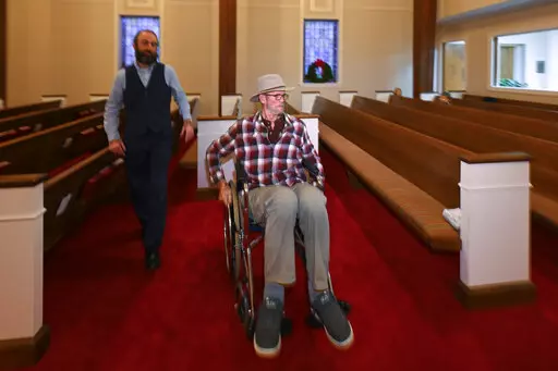Jerry Lamb, who has a spine condition, talks to Pastor Adam Kelchner at Camden First United Methodist Church Thursday, Dec. 8, 2022, in Camden, Tenn. The church at the urging of the pastor recently had a couple pews cut in half so Jerry, and anyone else who uses a wheelchair, walker or other aid, can still sit with the rest of the congregation. (AP Photo/John Amis)