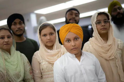 Amandeep Singh, 12, stands with his family in the communal room where "langar," food served after temple services, is provided at Guru Nanak Darbar of Long Island, a Sikh gurdwara, Wednesday, Aug. 24, 2022, in Hicksville, N.Y. Their Afghan Sikh family of 13 has found refuge in the diaspora community on Long Island where the Sikh community is helping family members obtain work permits, housing, healthcare and find schools for the children. (AP Photo/John Minchillo)
