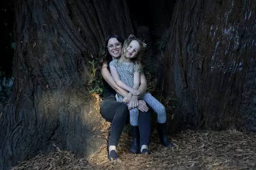 Hannah Levy holds her daughter, Aylah, 6, at Codornices Park, a location Aylah attended as a Berkeley Forest School student, during an interview in Berkeley, Calif., Wednesday, Nov. 8, 2023. Some parents like Levy don't see much value in traditional kindergarten. She wanted Aylah to enjoy being a kid. There is plenty of time, she reasoned, for her daughter to develop study skills. (AP Photo/Jeff Chiu)