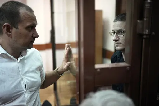 Robert Woodland, right, a Russia-born U.S. citizen, stands in a glass cage as he talks with his lawyer Stanislav Kshevitsky prior to a court hearing, Thursday, July 4, 2024, in Moscow, Russia. Woodland was convicted of drug-related charges and sentenced to 12 and a 1/2 years in prison on Thursday. (AP Photo/Alexander Zemlianichenko)
