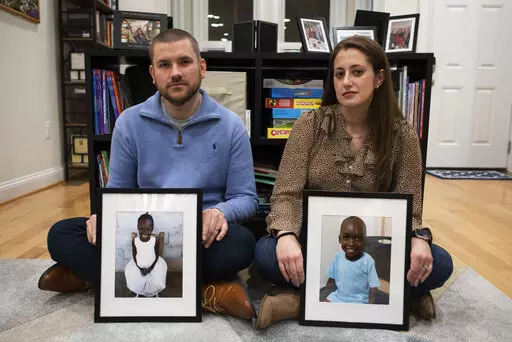 Bryan and Julie Hanlon hold photos of their adopted Haitian children, Gina, left, and Peterson, in a play area of their home in Washington, Tuesday, Feb. 7, 2023. They became the legal parents of the siblings in 2022 and fear they won't be able to secure their passports and fly them out of Haiti. (AP Photo/Cliff Owen)