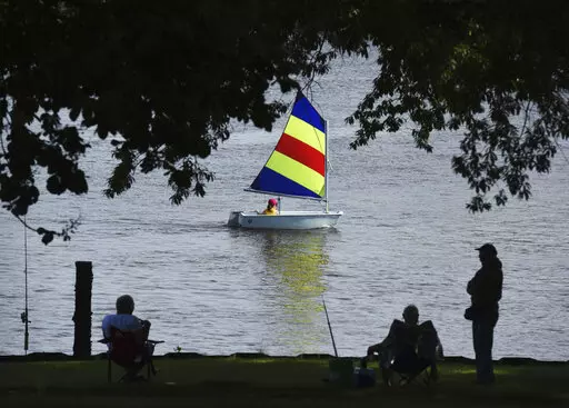 A sailor with the St. Joseph Junior Foundation Summer Sailling School cruises past fishermen along the St. Joseph River in St. Joseph, Mich., Wednesday, June 15, 2022.  The fast-changing coronavirus has kicked off summer in the U.S. with lots of infections but relatively few deaths compared to its prior incarnations. COVID-19 is still killing hundreds of Americans each day, but for many people the virus is not nearly as dangerous as it was.  (Don Campbell/The Herald-Palladium via AP)