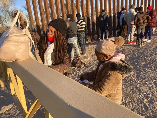 A Cuban woman and her daughter wait in line to be escorted to a Border Patrol van for processing in Yuma, Ariz., Sunday, Feb. 6, 2022, hoping to remain in the United States to seek asylum. For nationalities that don't need a visa, Mexico is often the ticket to seeking asylum in the United States. (AP Photo/Elliot Spagat)