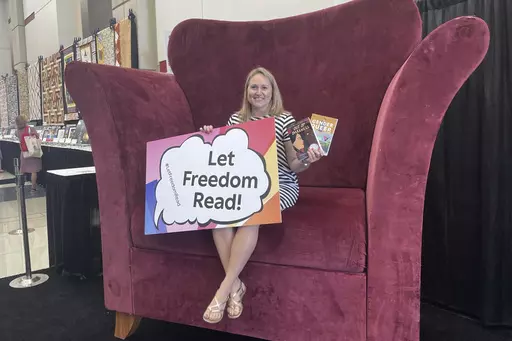 CORRECTS YEAR TO 2023 - School librarian Jamie Gregory, from South Carolina, displays two books that have been repeatedly challenged in the United States, while seated at the Banned Books from the Big Chair station at the American Library Association's annual conference in Chicago, June 24, 2023. The two books are: "Gender Queer," by Maia Kobabe, and "Out of Darkness," by Ashley Hope Pérez. (AP Photo/Claire Savage)